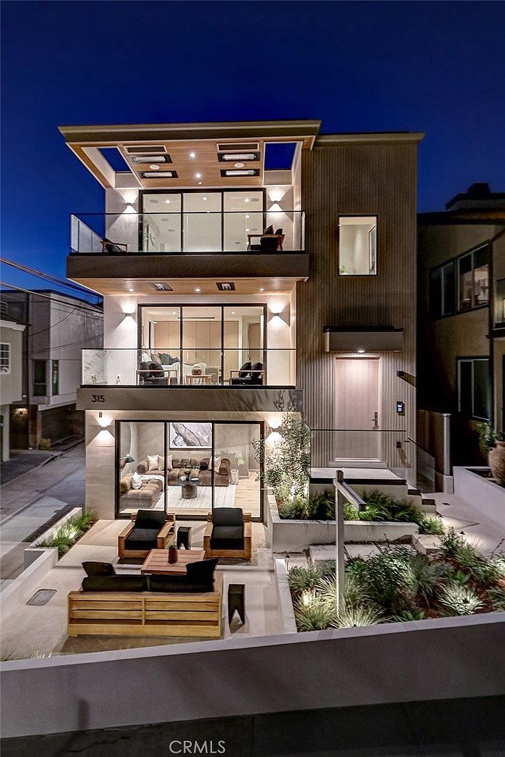 Twilight exterior with illuminated facade, glass balconies, and patio seating area